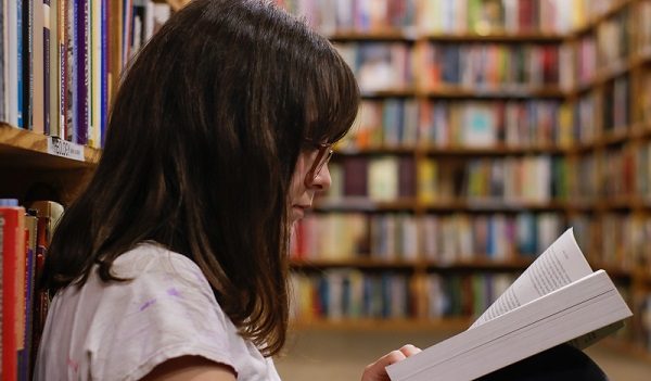 Foto di una ragazza che legge un libro in biblioteca